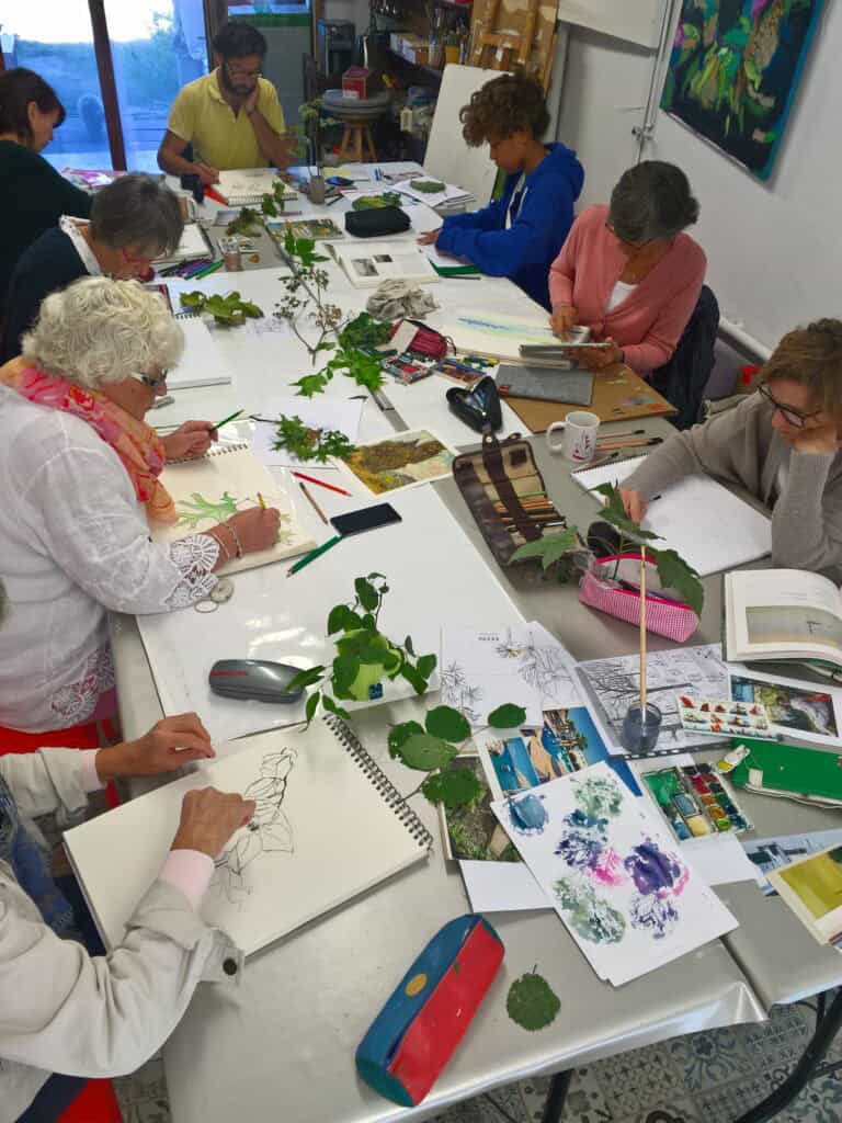 Photo d'un atelier adultes : personnes autour d'une table, dessinant des plantes dans des carnets.